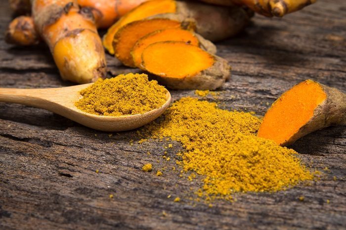Turmeric Powder In Spoon And Roots On Wooden Plate turmeric benefits for the skin